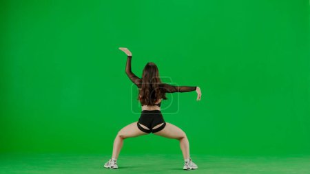 Téléchargez les photos : Dans le cadre sur fond vert, chromakey tient une jeune femme. Elle tourne le dos à la caméra, porte des vêtements révélateurs et fait la démonstration d'un mouvement de danse twerk. Elle est sexy, en plastique. - en image libre de droit