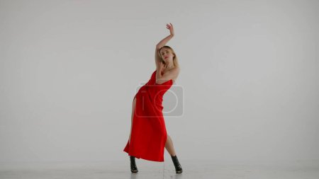 Téléchargez les photos : Encadré sur un fond blanc et gris. Jeune femme, montrant des mouvements de danse vers des talons hauts. Elle porte une belle robe rouge et des chaussures à talons hauts. Elle est sexy, rythmique, en plastique. Plan moyen. - en image libre de droit