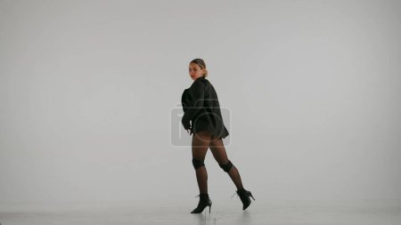 Foto de Enmarcado sobre un fondo blanco y gris. Mujer joven, demostrando movimientos de baile hacia tacones altos, en cuclillas. Ella está usando un hermoso vestido rojo y. Ella es sexy, rítmica, de plástico. Tiro medio. - Imagen libre de derechos