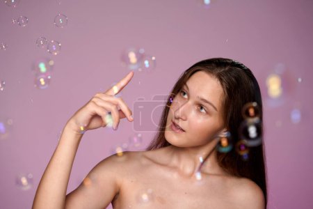 Téléchargez les photos : Femme attrayante s'amuser avec des bulles de savon. Portrait de la jeune femme séminude en studio sur fond rose dans un gros plan de bulles de savon. La féminité. Le concept de beauté, cosmétologie, soin de la peau - en image libre de droit