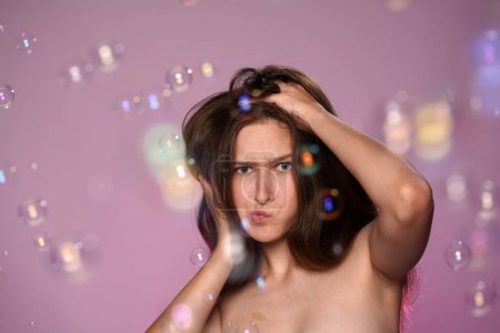 Foto de Una mujer joven tonteando, haciendo caras, follando con su cabello sedoso, liso y largo. Mujer Seminude en estudio sobre fondo rosa y luz de neón rosa rodeada de burbujas de jabón de cerca. El concepto de - Imagen libre de derechos