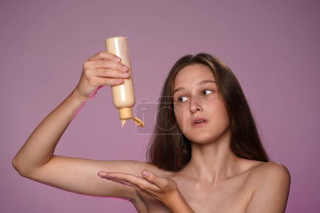 Foto de Una joven aprieta una crema, loción de una botella en la palma de su mano. Mujer Seminude en estudio sobre fondo rosa en luz de neón rosa de cerca. Crema para el cuidado de la piel. El concepto de belleza, cosmetología - Imagen libre de derechos