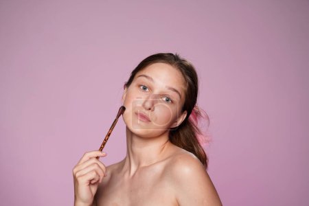 Téléchargez les photos : Femme appliquant le maquillage à l'aide d'une brosse de maquillage. Seminude femme en studio sur fond rose en néon rose de près. Contouring. Concept de beauté, cosmétologie, soin de la peau - en image libre de droit