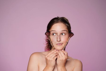 Foto de Mujer joven sosteniendo un cepillo de maquillaje de cerca. Mujer Seminude con piel clara y maquillaje desnudo en estudio sobre fondo rosa en luz de neón rosa. Maquillaje de contorno facial - Imagen libre de derechos