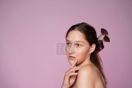 Foto de Retrato de mujer joven seminude en estudio sobre fondo rosa en luz de neón rosa de cerca. El cabello de las mujeres está cubierto con pinceles de maquillaje. Belleza, cosmetología, cuidado - Imagen libre de derechos