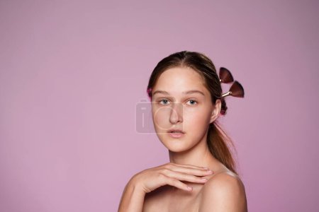 Téléchargez les photos : Portrait de jeune séminude femme en studio sur fond rose néon rose clair de près. Les cheveux des femmes sont épinglés avec des pinceaux de maquillage. Beauté, cosmétologie, soins - en image libre de droit