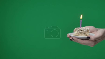 Photo for Close up on green chromakey background. A woman can be seen holding her hands. She is holding a piece of cake with candles and pointing at the camera. Its someones birthday, she says congratulations. - Royalty Free Image