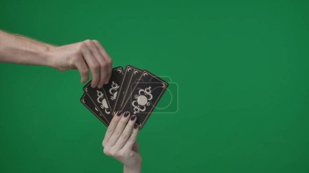 Photo for In a frame on a green background. A womans hand that holds a fan of tarot cards or playing cards, they are turned towards the camera with the outer side with a pattern. Someone is pulling one card. - Royalty Free Image