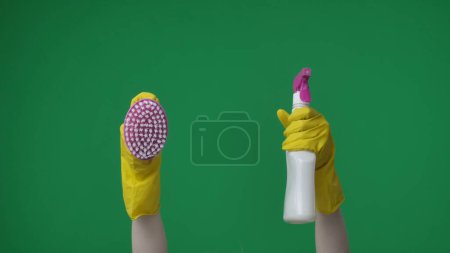 Foto de En el marco sobre un fondo verde, las manos femeninas cojas en guantes de goma amarillos sosteniendo un cepillo y detergente. Se utiliza para la limpieza y artículos de limpieza. Aquí puede estar tu publicidad. Marco medio. - Imagen libre de derechos