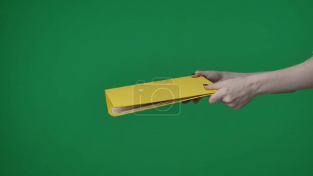 Téléchargez les photos : Dans le plan rapproché sur un fond vert, chromatique. La femme tient dans sa main un dossier jaune avec des documents. Elle l'étend à la caméra et la donne à quelqu'un. Cadre moyen. - en image libre de droit