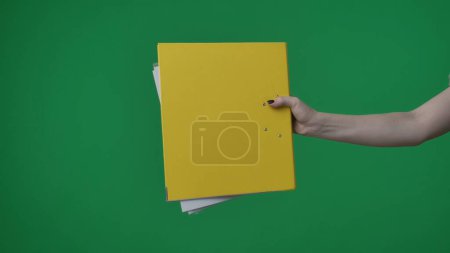 Photo for In the shot close up on a green background, chromakey. The woman holds in her hand a yellow folder with documents. She stretches it to the camera and gives it to someone. Medium frame. - Royalty Free Image