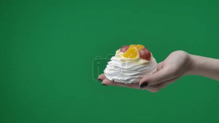 Photo for Close up on green chromakey background. A woman in the frame only her hands are visible. In her hand she has a cake, beautifully decorated with fresh fruits and berries. They are appetizing. - Royalty Free Image