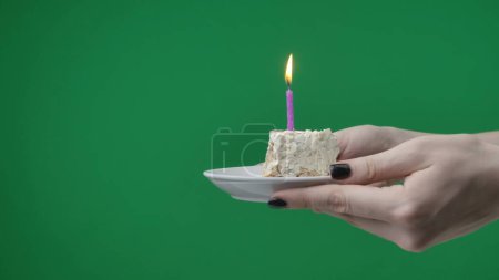Foto de Primer plano sobre fondo cromakey verde. Se puede ver a una mujer sosteniendo sus manos. Ella sostiene un pedazo de pastel con velas y señala a la cámara. Su cumpleaños someones, ella dice felicitaciones. - Imagen libre de derechos