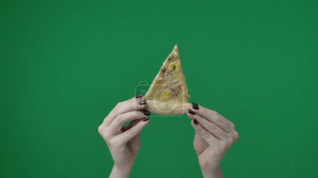 Téléchargez les photos : Gros plan sur fond vert chromatique. Main de femme, elle tient une tranche de pizza avec des garnitures les mains en l'air. Elle le montre à la caméra, le montre, le partage. - en image libre de droit