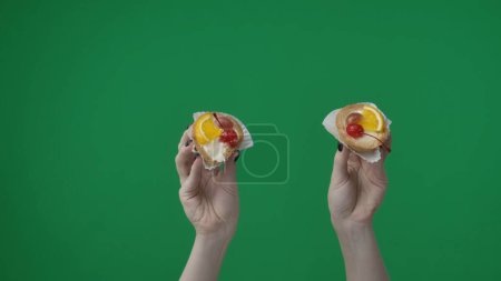 Photo for Close up shot on green chromakey background. The woman in the shot only her hands are visible. She is holding cakes with a beautiful decoration of fresh fruits and berries. Theye appetizing. - Royalty Free Image