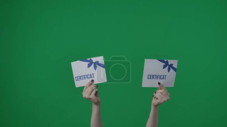 Photo for Framed on a green background, chromakey. A womans hand with a manicure holds a gift certificate for something. Perhaps someone won it, she hands it over, turning to the camera. Medium frame. - Royalty Free Image