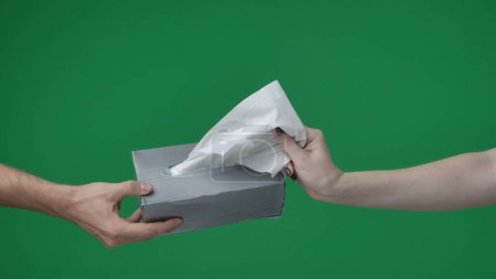Photo for In a close up shot on a green background, chromakey. Two people. A man holds and hands a box of tissues, a woman with a manicure extends her hand. Demonstrate the provision of assistance, care. - Royalty Free Image
