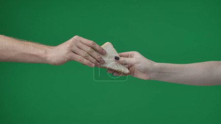Photo for In the shot close up on the green background. The womans hand holds two pieces of bread with a triangular shape. She reaches out to the man, who takes a pastry with a dark and light piece. - Royalty Free Image