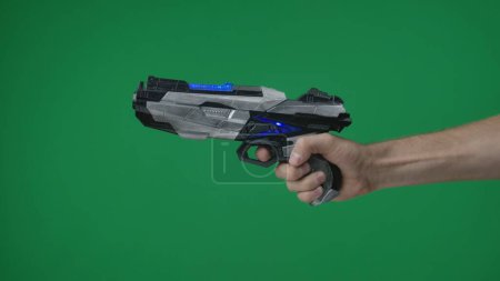 Photo for In a shot on a green background, a chromakey male hand that holds, holds out a plastic gun, a blaster, he pulls the trigger and points somewhere. Here can be your advertising. Medium shot. - Royalty Free Image