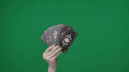 Photo for Framed on a green background, chromakey. A womans hand with a manicure holds playing tarot cards. She folded them like a fan and shows the outside with a beautiful pattern to the camera. Medium frame - Royalty Free Image