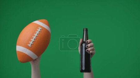 Foto de En el marco sobre fondo verde, cromakey manos femeninas con manicura sosteniendo una pelota de fútbol americano y una botella de vidrio de cerveza, alcohol. Aquí podría ser donde tu anuncio podría estar. Marco medio. - Imagen libre de derechos