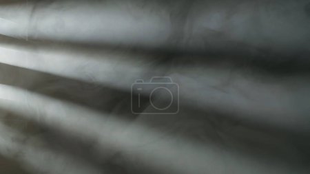 Téléchargez les photos : Des rayons de lumière provenant d'un projecteur à travers des châssis de fenêtre éclairent de près la fumée épaisse et dense ou le brouillard sur un fond noir. Fond abstrait de fumée et de brouillard - en image libre de droit