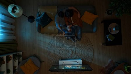 Photo for Top view shot of a homosexual couple sitting on the couch, watching TV together at night. One of them is frightened of the horror movie, their partner tries to comfort them. LGBT, equality, pride. - Royalty Free Image