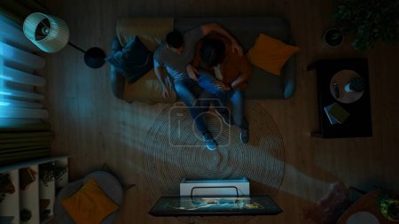Photo for Top view shot of a homosexual couple sitting on the couch, watching TV together at night. One of them is frightened of the horror movie, their partner tries to comfort them. LGBT, equality, pride. - Royalty Free Image