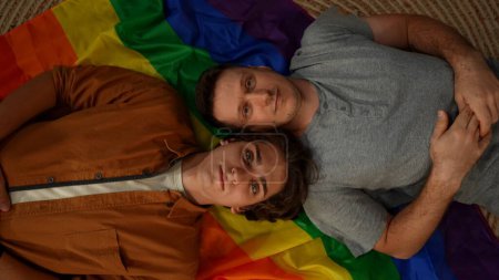 Téléchargez les photos : Vue de dessus d'un couple homosexuel, bisexuel, pansexuel et transgenre posé sur le drapeau LGBT, regardant la caméra pour encourager l'amour, l'égalité, la liberté. Contenu éducatif, liberté d'amour, fierté. - en image libre de droit