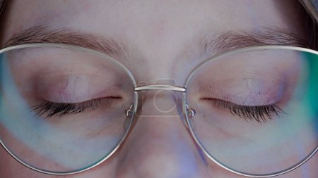 Téléchargez les photos : Les yeux fermés de la femme portant des lunettes macro shot. La lumière de l'ordinateur portable ou de l'ordinateur est réfléchie sur les lentilles des lunettes. Protégez vos yeux de la lumière bleue et des rayons - en image libre de droit