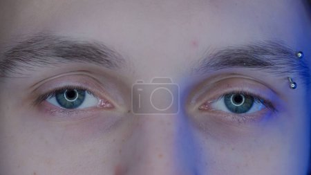 Téléchargez les photos : Yeux de jeune homme avec des sourcils piercing macro shot. Lumière bleue d'un smartphone, écran d'ordinateur se reflète dans les yeux mans. Le concept d'abus de gadgets - en image libre de droit