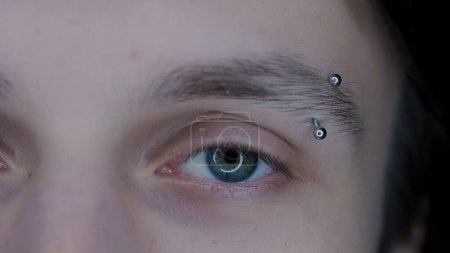 Téléchargez les photos : Œil de jeune homme avec des sourcils piercing macro shot. Elargissement des pupilles, dû à l'utilisation prolongée de gadgets. Syndrome des yeux secs. Concept de santé - en image libre de droit