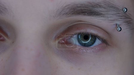 Téléchargez les photos : Œil de jeune homme avec des sourcils piercing macro shot. Elargissement des pupilles, dû à l'utilisation prolongée de gadgets. Syndrome des yeux secs. Concept de santé - en image libre de droit