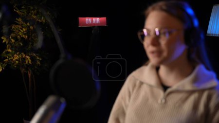 Photo for Beautiful young female dj speaks into microphone, records podcast or night news show for radio. Close up of podcast presenter or DJ talking on the microphone. Wears professional headphones. - Royalty Free Image