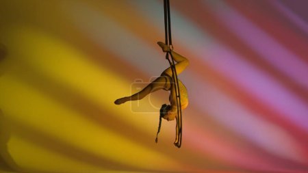 Foto de Chica de gimnasia rítmica realiza la escoria en un brazo en el aire en una luna estructura giratoria de metal. Fondo colorido. - Imagen libre de derechos
