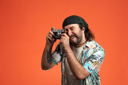 Téléchargez les photos : Un homme qui prend des photos sur une caméra rétro. Touriste masculin avec caméra en studio sur fond orange gros plan - en image libre de droit