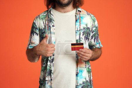 Photo for A man holds a credit card and shows thumbs up close up. Male traveler with a credit card in the studio on an orange background - Royalty Free Image