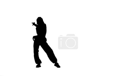 Photo for Framed against a white, light colored background in silhouette. A girl is dancing. She demonstrates various dance moves in jazz funk style. Only her outline is visible, she is alone. General plan. - Royalty Free Image