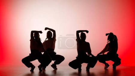 Foto de En el marco sobre un fondo rojo, blanco, degradado. Grupo de baile compuesto por chicas atractivas, en silueta. Demuestran movimientos de baile en la dirección del jazz funk - Imagen libre de derechos