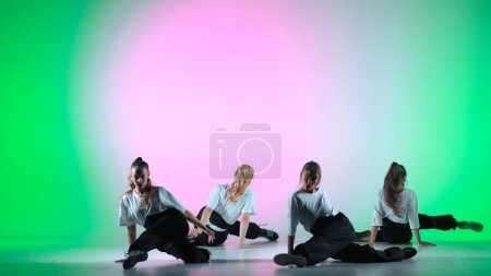 Photo for In the frame on a green, gradient background in the spotlight. A group of attractive, young girls is dancing. They demonstrate various dance moves in the direction of jazz funk - Royalty Free Image