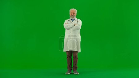 Photo for Healthcare and wellness creative concept. Portrait of man medic in studio on chroma key green screen. Senior doctor in white uniform standing with crossed arms and smiling. - Royalty Free Image