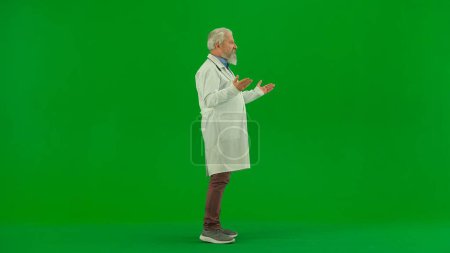 Photo for Healthcare and wellness creative concept. Portrait of man medic in studio on chroma key green screen. Senior doctor in white uniform standing and talking, gesturing with hands. - Royalty Free Image
