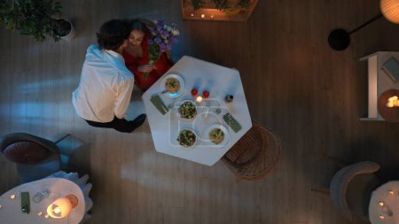 Téléchargez les photos : Dans la photo ci-dessus, un jeune couple aimant est assis dans un café, un restaurant. Désigne une date, l'homme lui tend un bouquet de fleurs et l'embrasse. Elle se réjouit. A proximité sur la table sont différents plats. - en image libre de droit