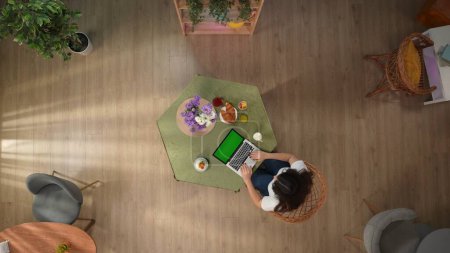 Photo for In the top frame there is a young girl sitting at the table in the cafe. She is typing, looking at a laptop with a green screen. Theres dessert on the table, and a glass of juice. - Royalty Free Image