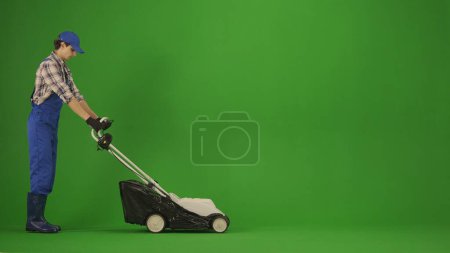Photo for Agriculture and natural farming creative advertisement concept. Portrait of farmer in working clothing on chroma key green screen. Gardener standing and mowing the grass with petrol lawn mower. - Royalty Free Image