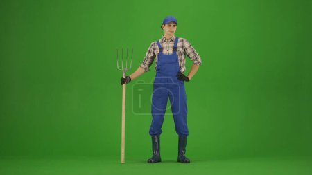 Photo for Agriculture and natural farming creative advertisement concept. Portrait of farmer in working clothing on chroma key green screen. Gardener standing posing at the camera with pitchfork. - Royalty Free Image