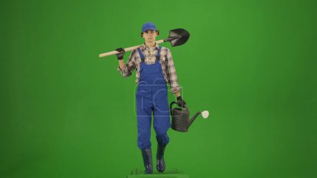 Photo for Agriculture and natural farming creative advertisement concept. Portrait of farmer in working clothing on chroma key green screen. Gardener walking holding shovel over shoulder and watering can. - Royalty Free Image