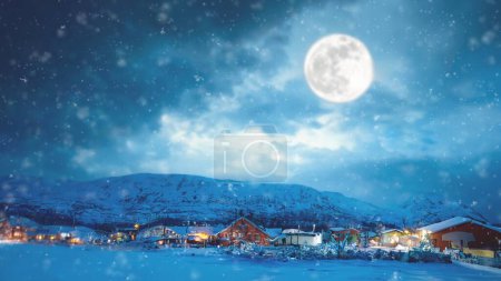 Téléchargez les photos : Village d'hiver dans les montagnes. Beau paysage de Noël. Il y a une pleine lune dans le ciel et il neige - en image libre de droit