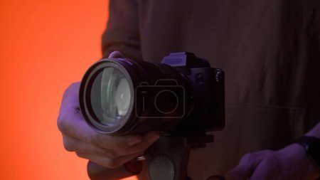 Foto de La cámara fotográfica profesional se encuentra en un trípode en un estudio con iluminación de neón de color. El fotógrafo hace ajustes antes de que comience el rodaje - Imagen libre de derechos