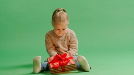 Photo for Portrait cute little girl kid holding gift box posing isolated over yellow background wall in studio. Magic light comes from the box. Christmas concept. - Royalty Free Image